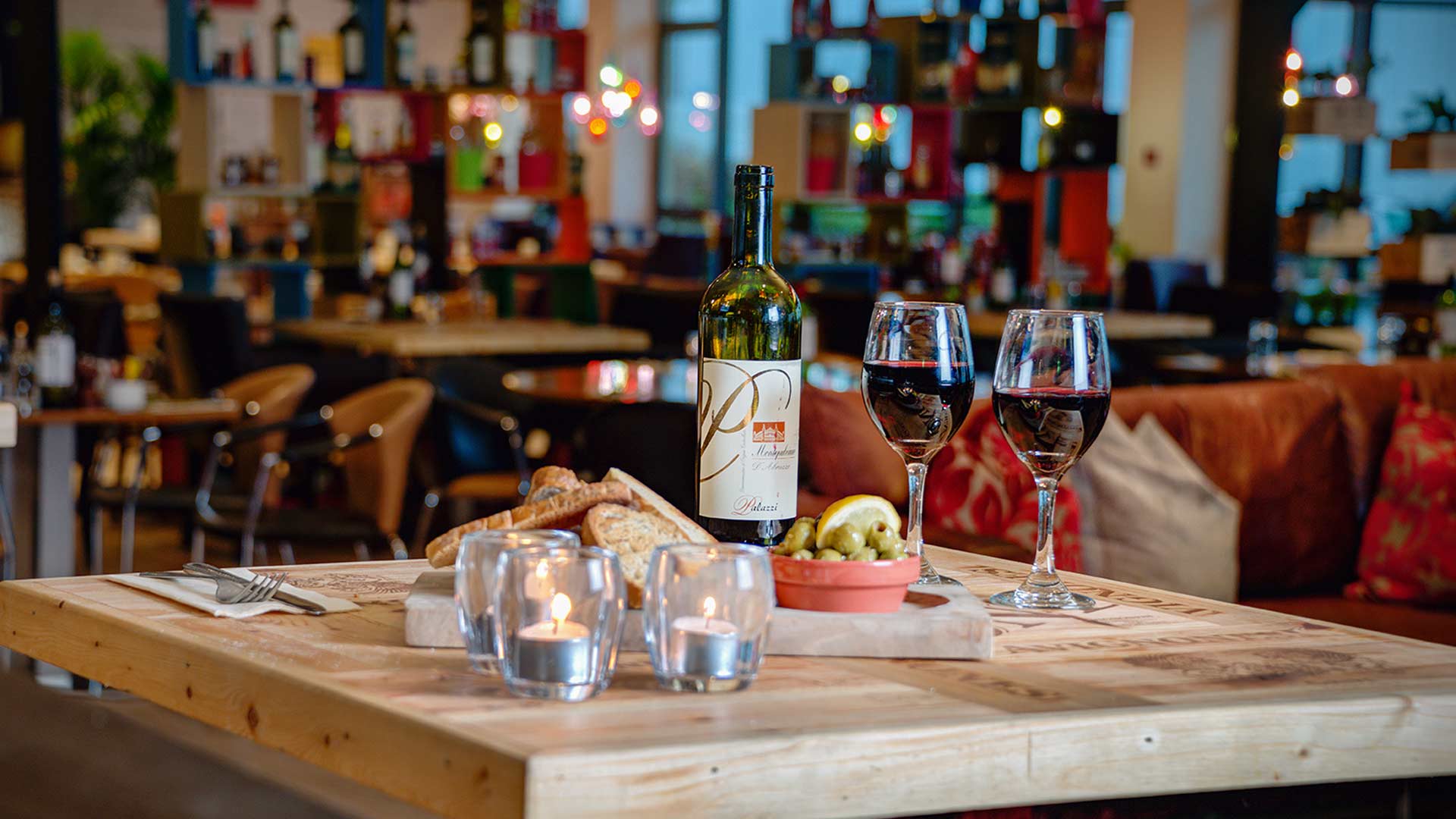 Table set with red wine, toasted crusty bread, candles and olives in the romantic surroundings of the Olivo Eatery
