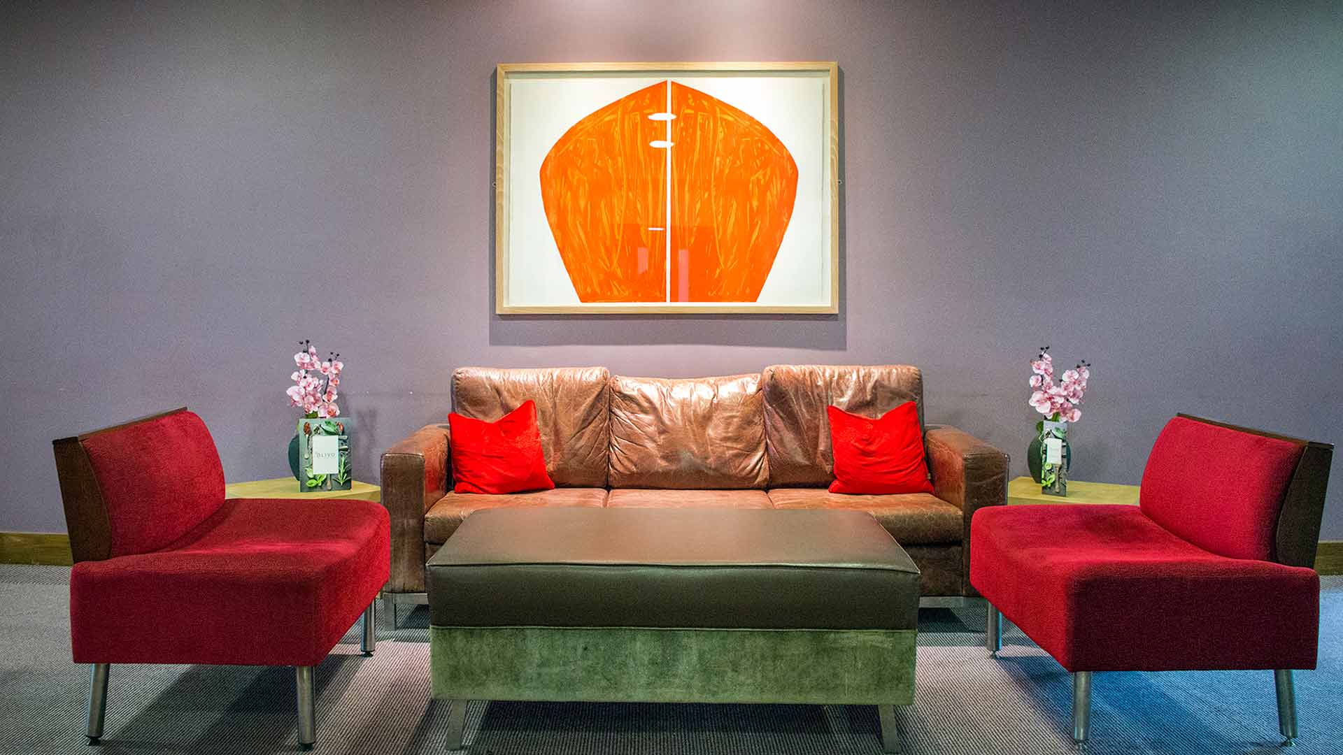 Stylish seating area with a leather sofa, velvet red chairs and striking abstract art at the Cork Airport Hotel