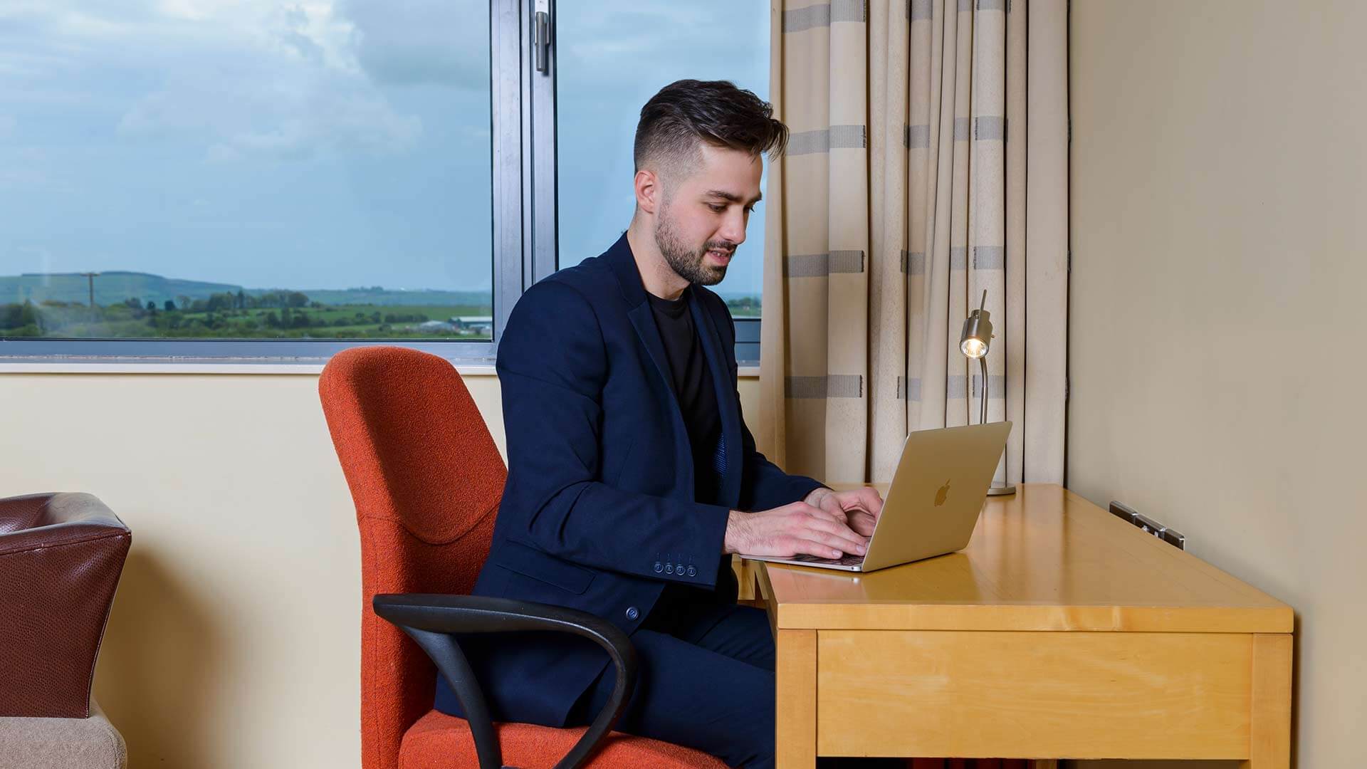 Man sitting at desk in hotel room typing on a laptop