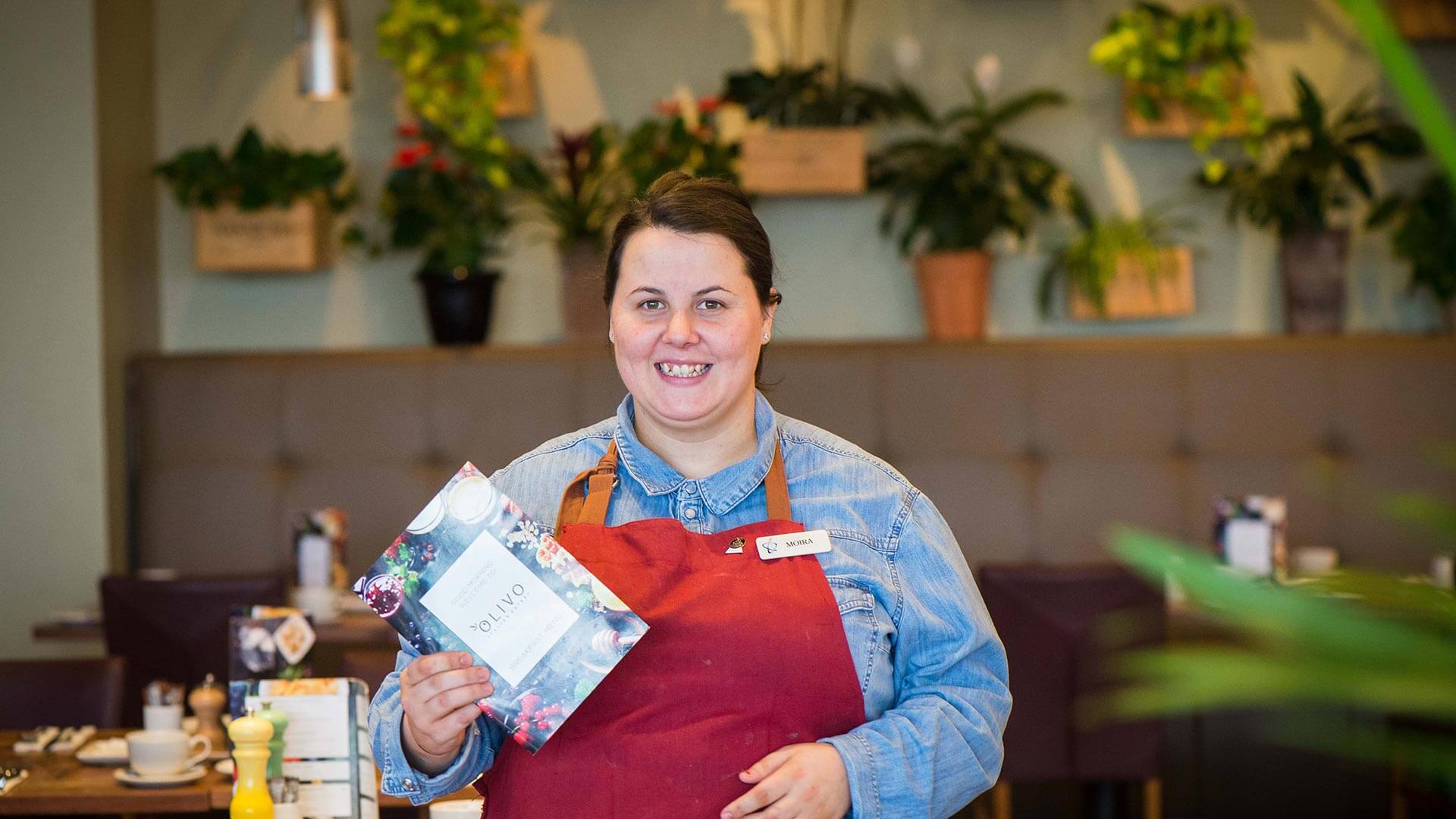 Member of staff at Cork Airport Hotel, in the dining area, holding a menu